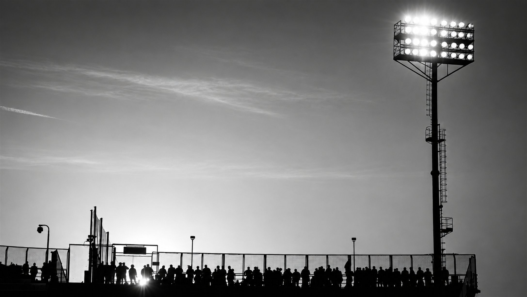 Silhueta de torre de holofotes e torcida em um estádio, em preto e branco